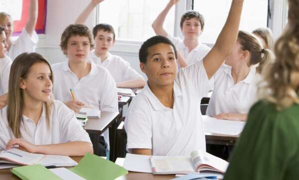 secondary school pupils with hands up in classroom 0