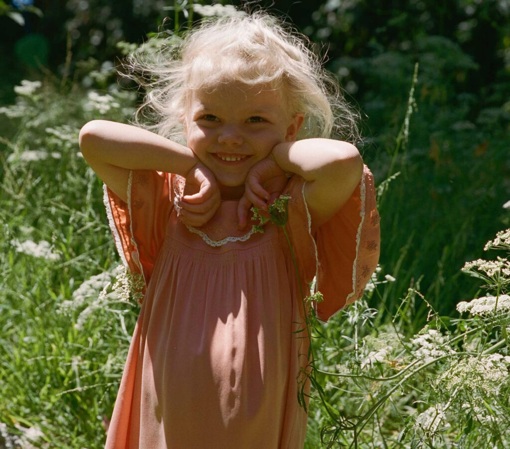 Bimba felice, sorride, in mezzo al campo, col vestito nuovo, color papaya